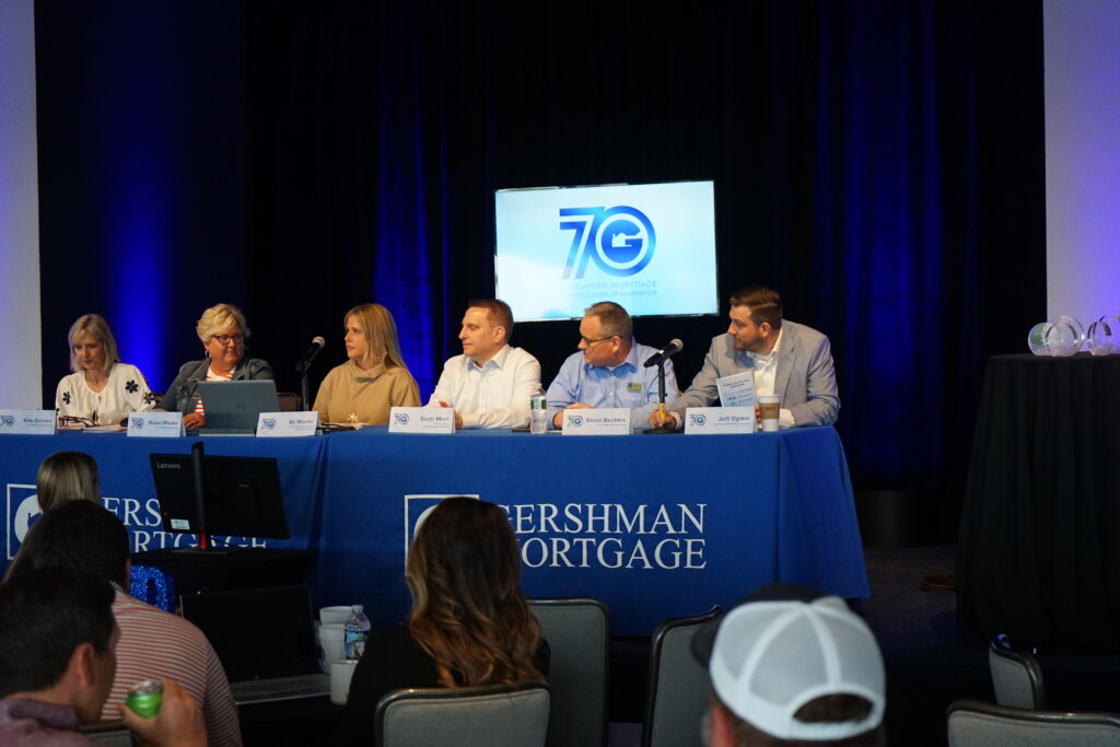 A panel of six Gershman Mortgage professionals seated at a table on stage, speaking to an audience, with branded signage and awards visible nearby.