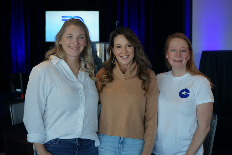 3 women standing in a meeting room and smiling at a camera