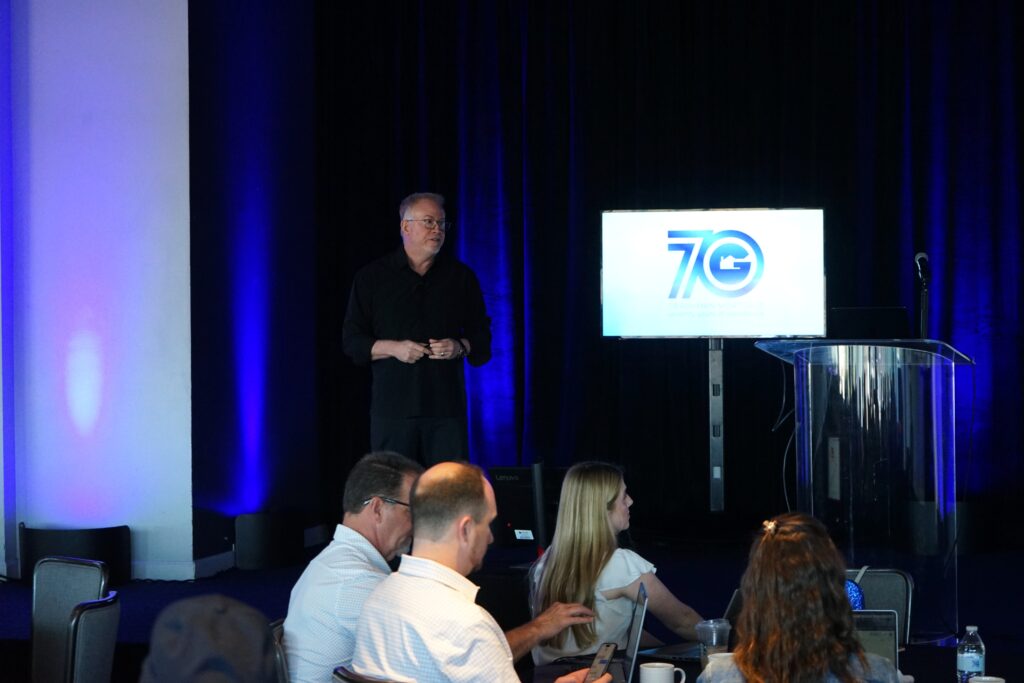 Dave Savage on stage in front of a Gershman Mortgage 70th Anniversary Logo, giving a speech. 