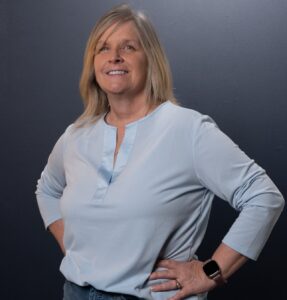 Jamie Burk in a powder blue shirt, standing up and looking at the camera while smiling