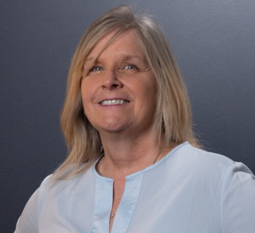 Jamie Burk in a powder blue shirt, standing up and looking at the camera while smiling